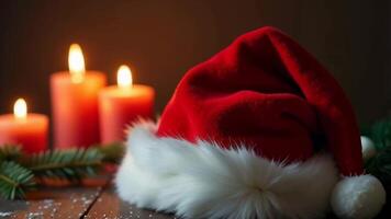 A Santa hat rests beside lit candles and pine branches, creating a warm video