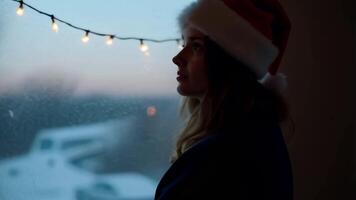 A mysterious silhouette of a person in a red Santa hat stands by a frosty window or near a Christmas tree video