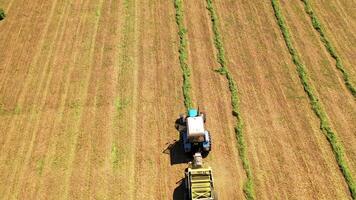 Drone view of agricultural machine working on the field. Tractor collects dried grass for feeding livestock. Motion camera bottom up. video