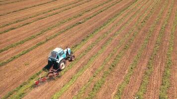 Aerial panoramic view of a huge field with agricultural works. Tractor scatters grass in a sunny summer day. Camera moves bottom up. video