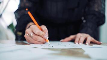 Hands of a professional tailor is drawing a sketch with a sharp pencil on a table. Dressmaker is making a creative design of a dress on a sheet of paper in her workplace. video