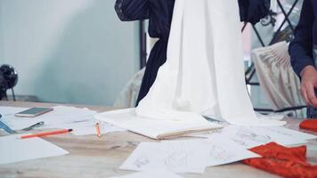 Two dressmakers are laying out new cloth on the table. White and red fabric in the hands of professional seamstresses in atelier. Tailors prepares material for sewing dresses in workshop. video