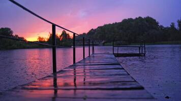 Heavy rain with small lightning over the river. Long footbridge in the river during the rain in the evening in summer. Beautiful natural background at sunset with rainy drops outdoors. video