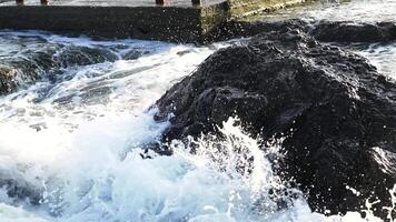 Sea waves hit the rocks and fly around with a lot of splashes. Big wave crashing into the big rock and becomes the white foam. Awesome power of waves breaking over dangerous rocks video