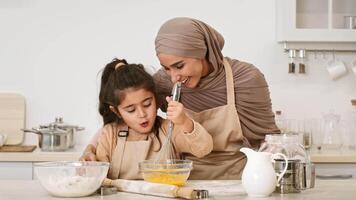 In a warm and inviting kitchen, a mother helps her daughter whisk eggs, creating a joyful moment filled with laughter and learning. Their shared experience emphasizes family bonding. video