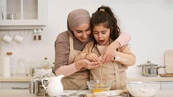 A mother and her daughter are happily cooking together in a modern kitchen, sharing laughter while cracking eggs into a bowl. Their hands work in unison, creating a warm moment. video