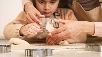 A child and her mother are engaged in baking, using cookie cutters to shape dough on a floured countertop. The atmosphere is warm and inviting as they enjoy the activity together. video