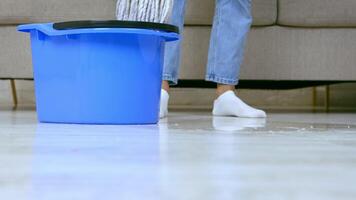 A person is actively mopping the floor with a blue bucket and cleaning cloth, ensuring their living room remains tidy. The effort is focused on maintaining a clean and organized space. video