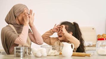 A mother and her daughter playfully interact while preparing a meal in a sunny kitchen. They laugh and make funny faces, creating a delightful bonding experience during cooking. video