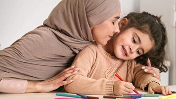 A mother and her daughter share a joyful moment as they draw with colored pencils. The daughter focuses intently on her artwork, while the mother leans in affectionately. video
