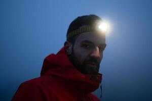 Hiker or triathlon trail runner with a headlamp on a trail in the mountain with fog at night photo