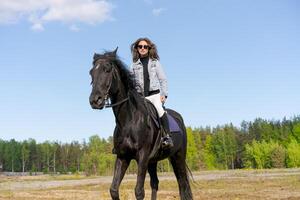 Woman is riding a black horse in a field photo