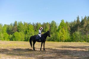 Woman is riding a horse in a field with trees in the background photo