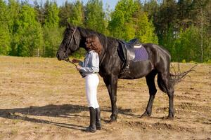 Woman is standing next to a black horse in a field photo