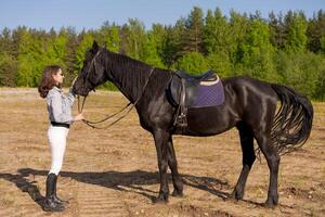 Woman is standing next to a black horse photo
