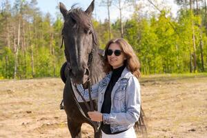 Woman is standing next to a black horse photo