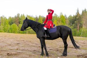 Man in a red coat is riding a black horse in a field photo