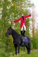 Woman is standing on top of a black horse in a forest photo