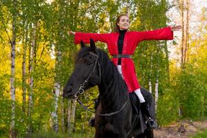 Woman is riding a black horse in a forest photo