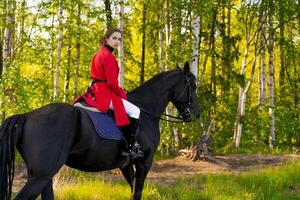 Woman is riding a black horse in a forest photo