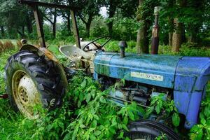 An old blue tractor is sitting in the grass photo