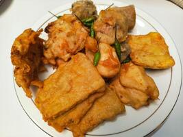 photo of a typical Indonesian snack plate consisting of fried tofu, fried tempeh, bakwan and fried banana placed on a white plate