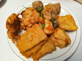 photo of a typical Indonesian snack plate consisting of fried tofu, fried tempeh, bakwan and fried banana placed on a white plate