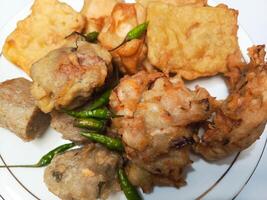 photo of a typical Indonesian snack plate consisting of fried tofu, fried tempeh, bakwan and fried banana placed on a white plate