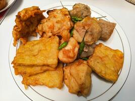 photo of a typical Indonesian snack plate consisting of fried tofu, fried tempeh, bakwan and fried banana placed on a white plate