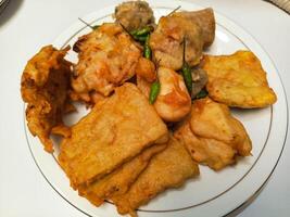 photo of a typical Indonesian snack plate consisting of fried tofu, fried tempeh, bakwan and fried banana placed on a white plate
