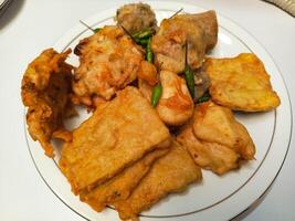 photo of a typical Indonesian snack plate consisting of fried tofu, fried tempeh, bakwan and fried banana placed on a white plate