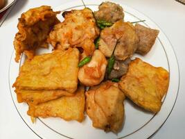 photo of a typical Indonesian snack plate consisting of fried tofu, fried tempeh, bakwan and fried banana placed on a white plate