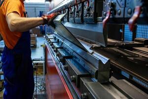 Worker adjusts a large metal sheet on an industrial press, ensuring precision in a busy manufacturing environment. photo