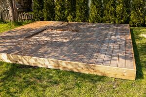 Wooden deck with central sandpit in a backyard setting, surrounded by trees and natural surroundings photo