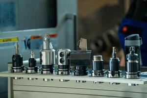 A row of various metalworking tools including drill bits and milling cutters on a workbench in a well organized metalworking factory with industrial machinery in the background. photo