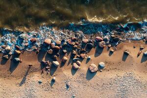 large rocks scattered along the sandy beach with waves crashing over them photo