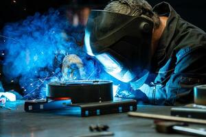 Close up of a welder focused on his work, bright blue light and sparks emanating from the welding torch. photo