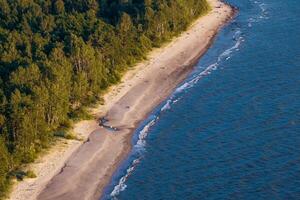 long, narrow beach bordered by dense forest on one side and a calm ocean on the other, captured from an aerial perspective photo