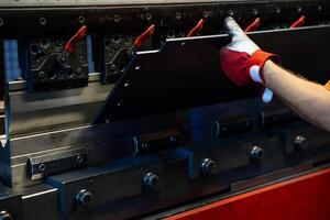 Close up of a worker's gloved hand adjusting metal components in an industrial press machine, emphasizing precision and control. photo