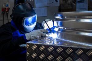 Welder with protective gear welding a metal structure in a workshop, focusing on the bright welding light and precision work. photo