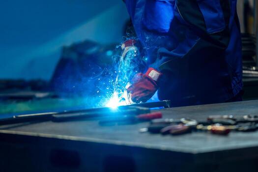 Welder using a torch, bright blue flame and sparks in a workshop, creating a strong weld on metal. photo