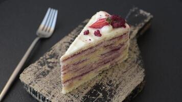 Piece of sweet layer cake with white cream, raspberries and strawberries on a dark concrete background video