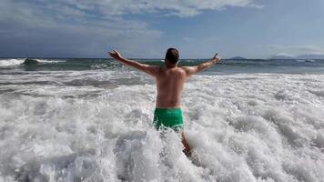 A Caucasian man joyfully embraces ocean waves at the beach, symbolizing freedom and summer vacations video