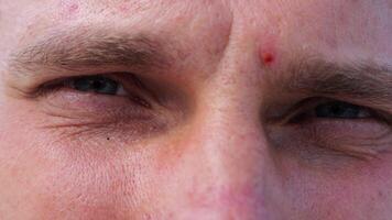 Close up to upset male face looking into camera with a disappointing sight. Upset facial expression of man with blue eyes. Unhappy gaze of despairing young guy. Slow motion video