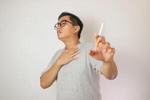 Smoker holding a cigarette suffering from chronic cough, Asian man patient coughing with respiratory problems, emphysema disease or lung cancer from smoking, medical and health care concept. photo
