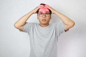 A man in a grey shirt holds his head with a pained expression, indicating a headache or discomfort. The plain light blue background emphasizes his distress and highlights his posture and expression photo