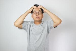 Portrait of young man isolated on gray background, suffering from severe headache, pressing fingers to temples with closed eyes photo