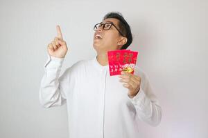 Smile face of Asian man wearing Chinese traditional cloth called Cheongsam pointing to an angpao and looking at the camera on white background photo
