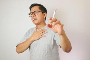 Smoker holding a cigarette suffering from chronic cough, Asian man patient coughing with respiratory problems, emphysema disease or lung cancer from smoking, medical and health care concept. photo