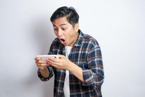 Portrait of attractive Asian man playing games on his mobile phone by tilting the screen. Wow face expression. Isolated image on gray background photo